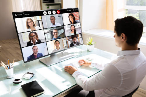 a man at a computer on a sunny day with a 30% POP in a virtual conference with nine smiling people on his 47" screen. 