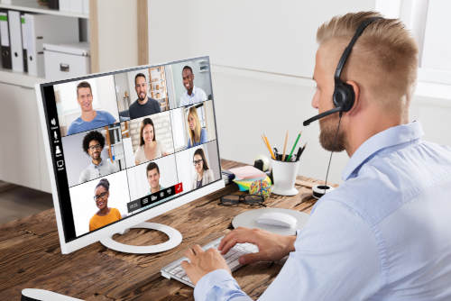 a man at a home office in a video conference with other participants on his screen