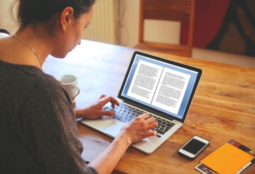A woman sits at a computer typing up a report.