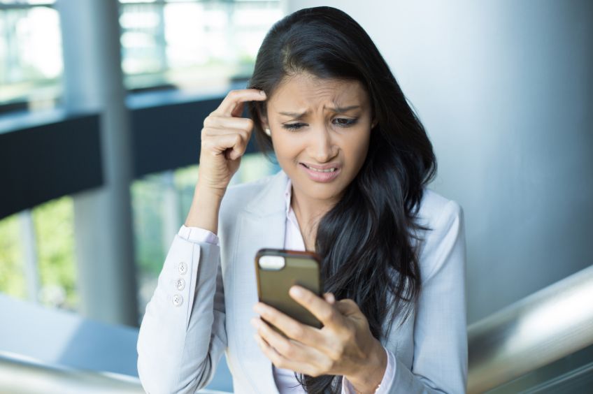 business woman looking confused as she reads misused words in an email on her mobile phone 