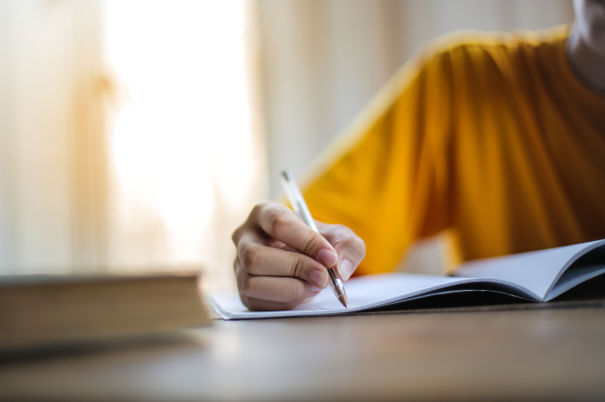 Zoomed in image of a woman's arm writing on paper with a pen