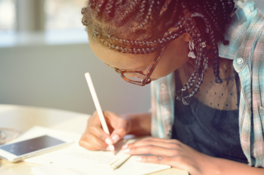 zoomed in image of a woman writing on paper with a pen